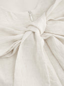 Woman wearing an ivory boat-neck mini dress with a knotted backless detail