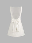 Woman wearing an ivory boat-neck mini dress with a knotted backless detail