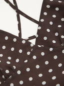 Woman wearing a dark brown polka dot midi dress with a matching scarf