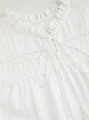 Woman wearing a white cotton mini dress with lace insets and puff sleeves