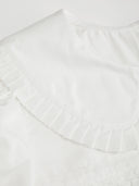Woman wearing a white babydoll mini dress with a Peter Pan collar and puff sleeves