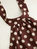 Woman wearing a chocolate brown polka dot halter mini dress with an open back