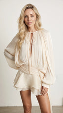 Woman wearing an ivory pleated bishop sleeve mini dress with matching shorts