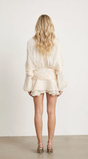 Woman wearing an ivory pleated bishop sleeve mini dress with matching shorts
