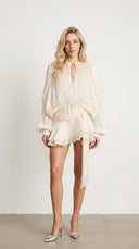 Woman wearing an ivory pleated bishop sleeve mini dress with matching shorts