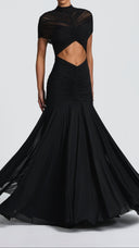 Woman wearing a black ruched cape maxi dress, side view showing the flared skirt