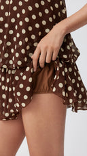 Woman wearing a chocolate brown polka dot halter mini dress with an open back
